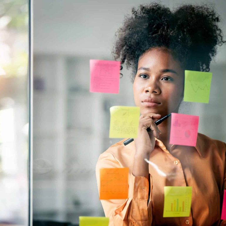 Frau die vor einer Glaswand mit Notiz-Zetteln steht und nachdenkt